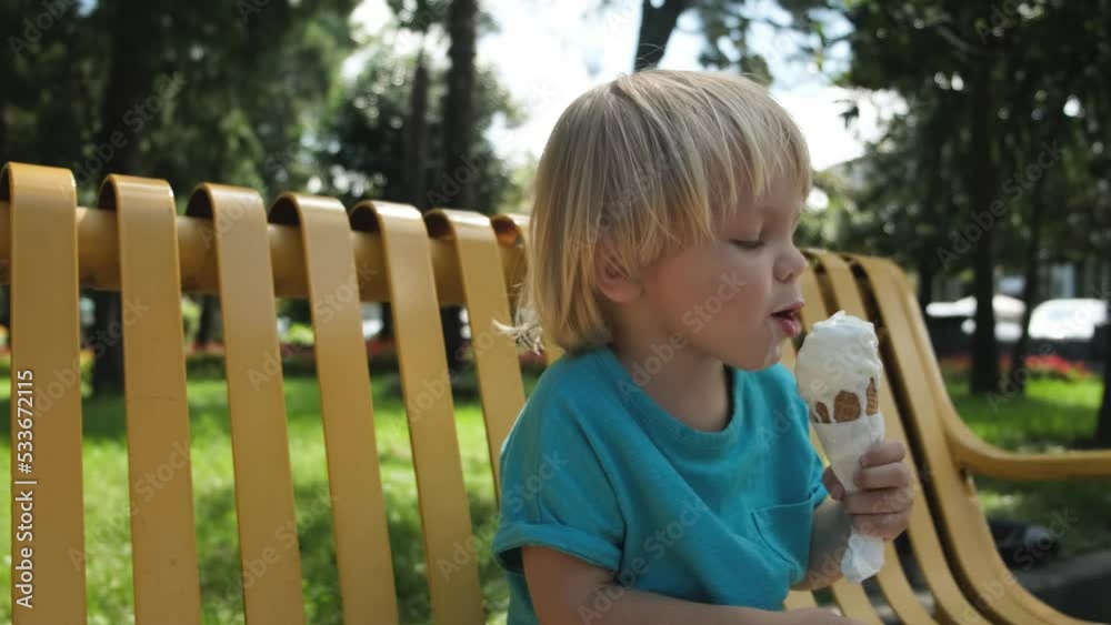 a small child eats ice cream cone sitting on a yellow bench in the park a small child eats ice cream cone sitting on a yellow bench in the park