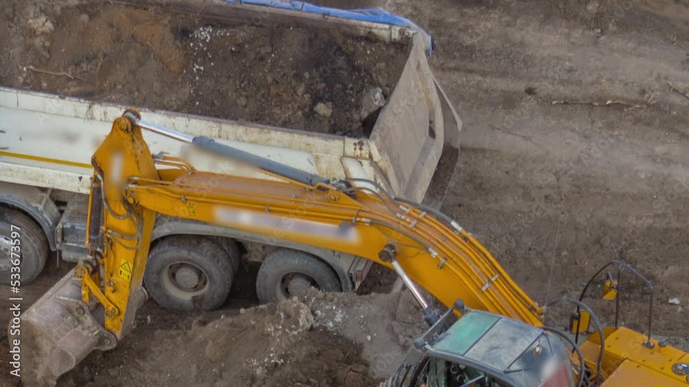 Close up view of Industrial truck loader excavator moving ground and loading into a dumper truck timelapse on road construction site. Aerial view of reconstruction of tram tracks Close up view of Industrial truck loader excavator moving ground and loading into a dumper truck timelapse on road construction site. Aerial view of reconstruction of tram tracks