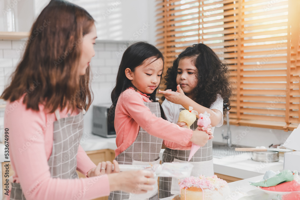 Children enjoy cooking in the kitchen. Happy Asian kids decorating the cake, bake cookies in the kitchen. Two cute little diversity girls play and learn trough the experience. Education concept.