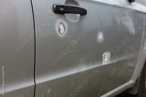 A part of a gray car damaged by fragments from military missiles, puttied parts, holes smeared with putty,