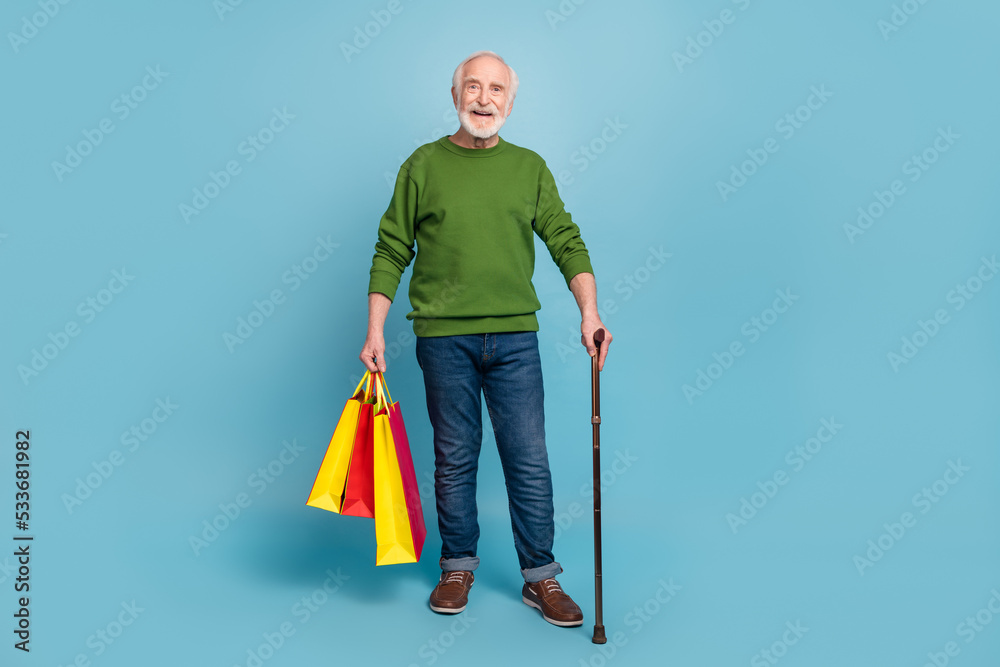 Full body photo of positive cheerful aged person hold boutique packages isolated on blue color background Full body photo of positive cheerful aged person hold boutique packages isolated on blue color background