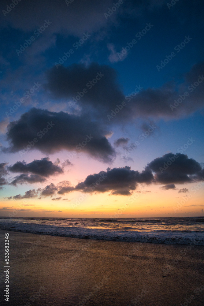 Beautiful sunset sunrise at the beach with dramatic clouds in the blue purple yellow sky over the sea - Bali