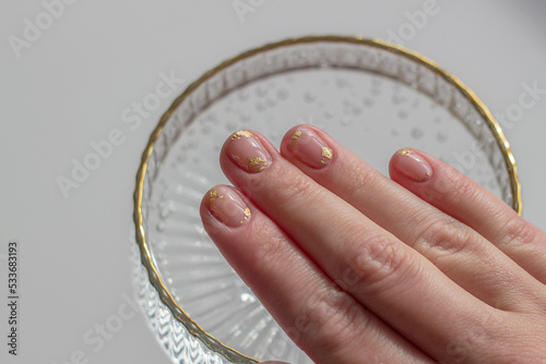gentle aesthetic trendy manicure on short nails with transparent gel polish with decor pieces of gold foil close-up on fingernails