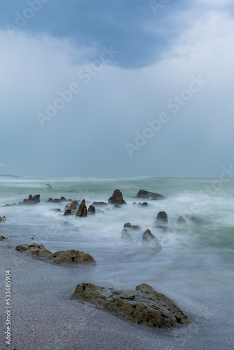 Moody Skulpiesbaai seascape under a brooding sky, the water and waves blurred because of long exposures. Hermanus, Whale Coast, Overberg, Western Cape, South Africa.
