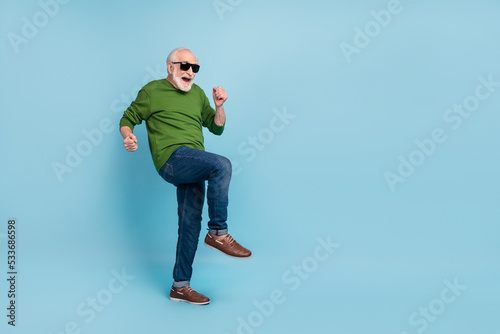 Full size portrait of overjoyed glad aged man raise fists dancing have fun isolated on blue color background