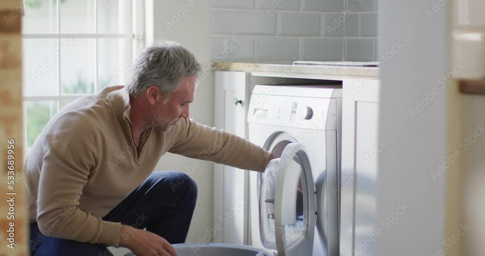 Happy caucasian man holding basket and doing laundry in kitchen