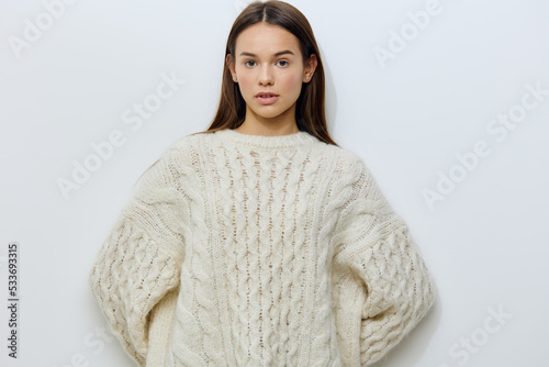 attractive, young woman stands in a white stylish sweater on a light background pleasantly looking at the camera with well-groomed hair