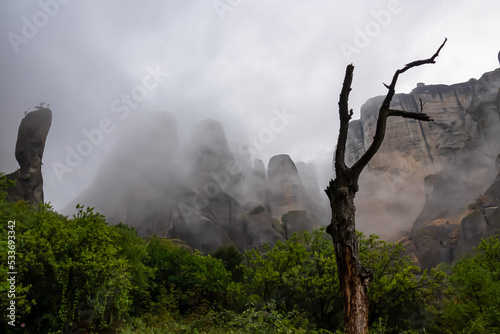 Panoramic view of unique rock formations near rock Aghio Pnevma (Holy Spirit) on cloudy foggy day in Kalambaka, Meteora, Thessaly, Greece, Europe. Tree standing in the middle surrounded by fog photo