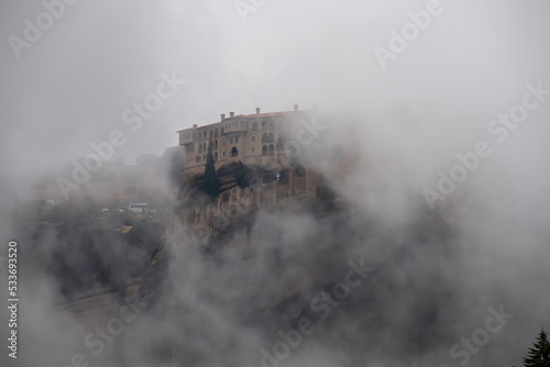 Panoramic view of Holy Monastery of Varlaam surrounded by misty fog on cloudy day  Kalambaka  Meteora  Thessaly  Greece  Europe. Dramatic landscape appearing. Landmark build on unique rock formations