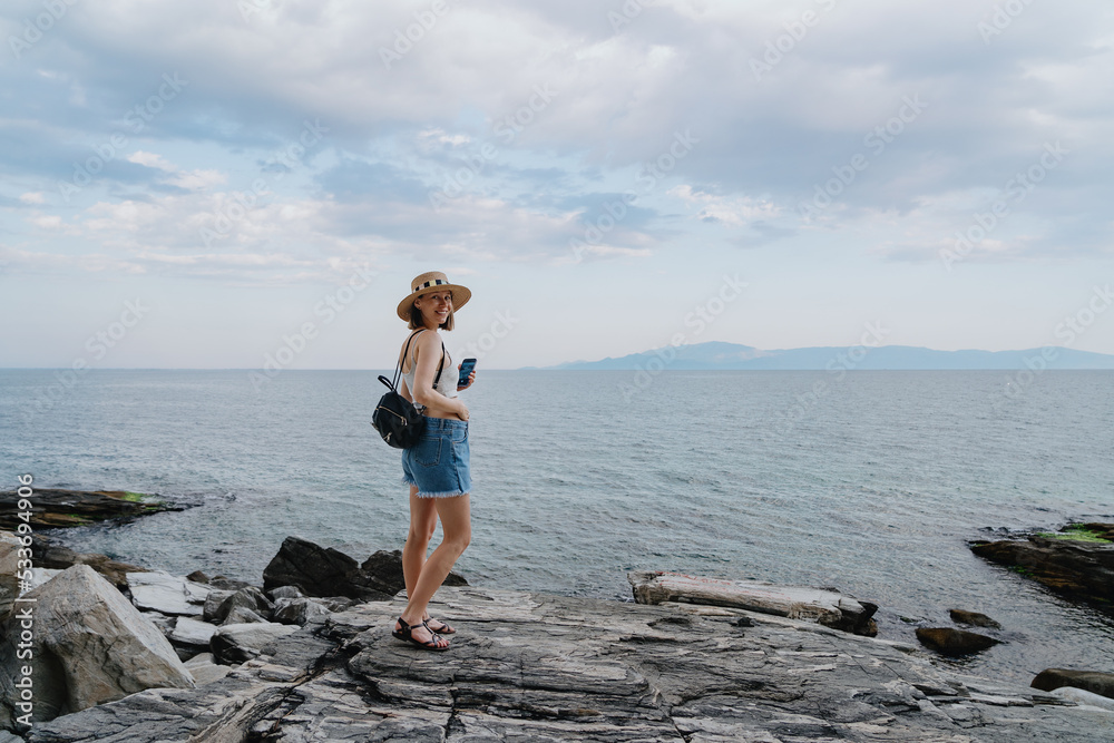 Woman traveler, backpacker, taking pictures with smartphone, while exploring Greek sea