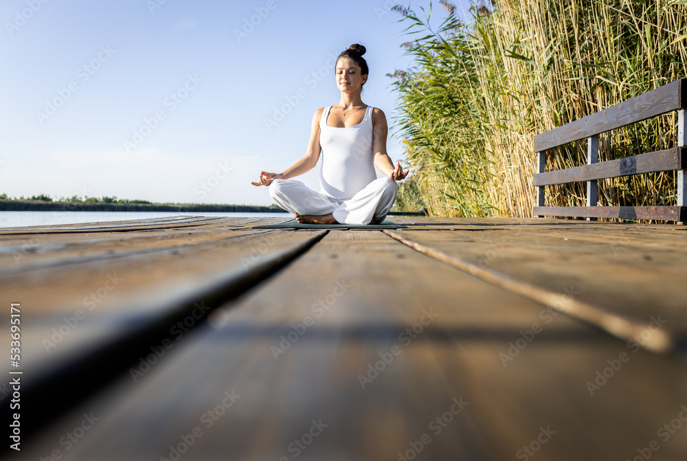 Pregnant woman doing yoga at lake during the day.