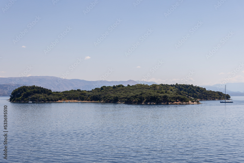 Protected nature reserve wooded uninhabited Ptichia island is located in the bay opposite Corfu Town, Ionian islands, Greece, background in summer haze
