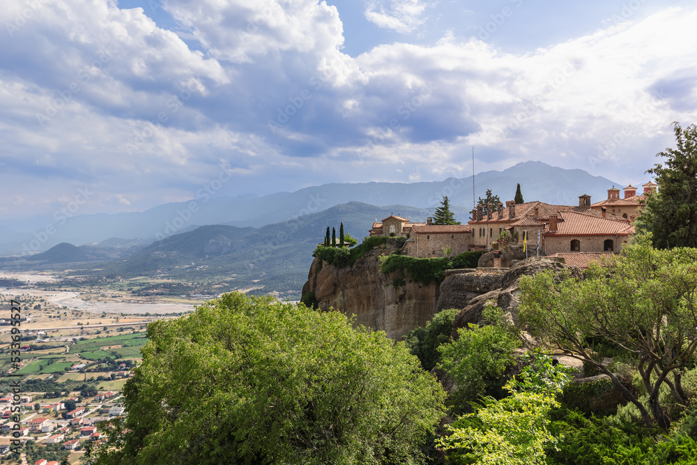 Panoramic view of ancient St. Stephen Holy Monastery with unique sheer cliffs and dense green forest in Thessaly plain, Meteora, Greece