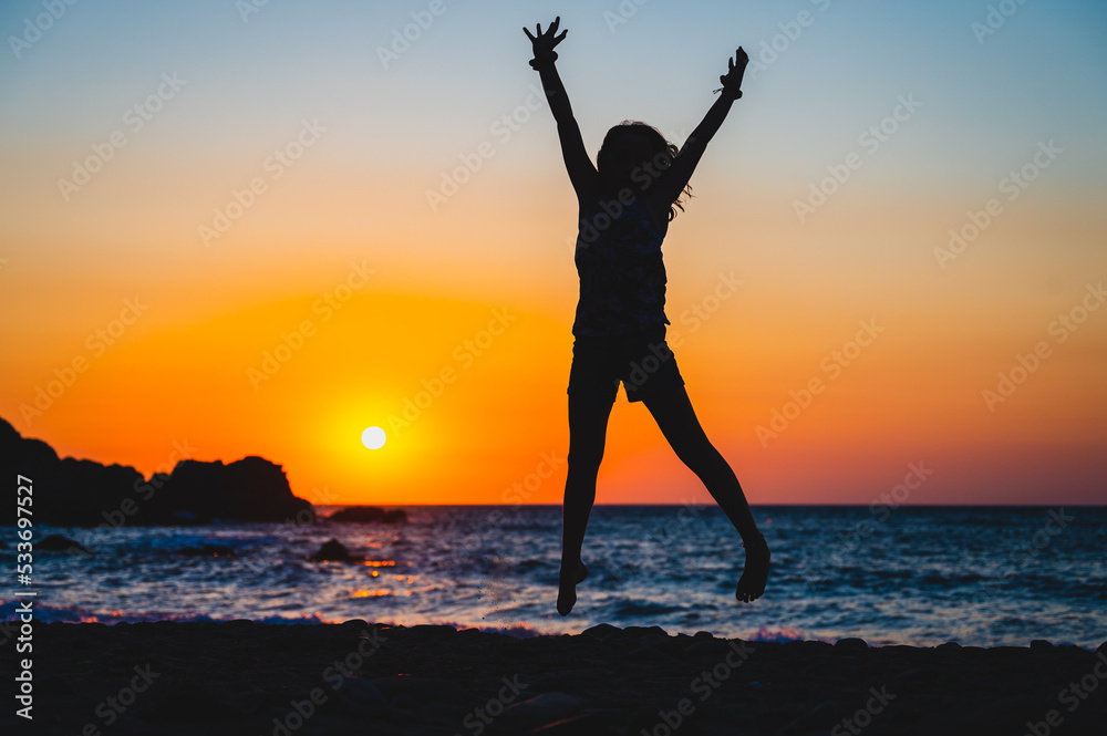 Silhouette of a child jumping in sunset on a beach.