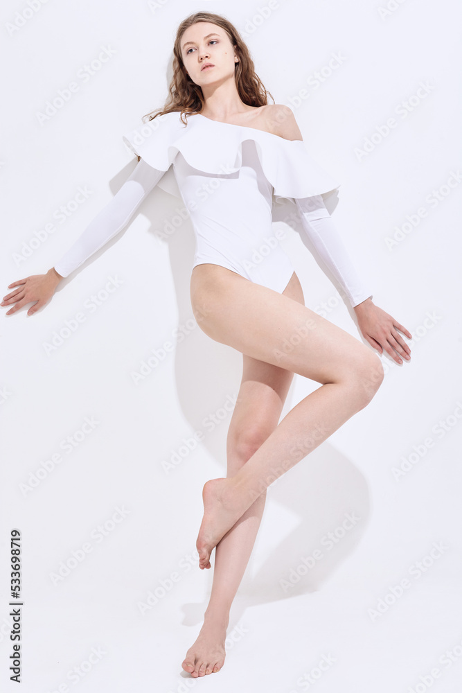 a beautiful slender woman in a white swimsuit poses on a light background a beautiful slender woman in a white swimsuit poses on a light background