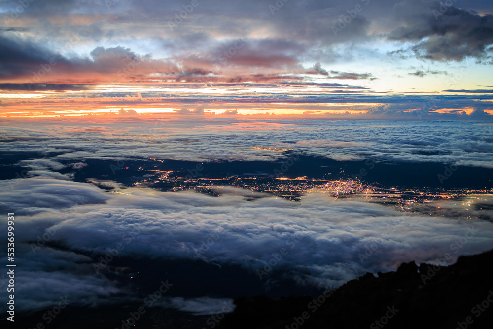 Looking down on clouds and city lights from top of Mt. Fuji before sunrise