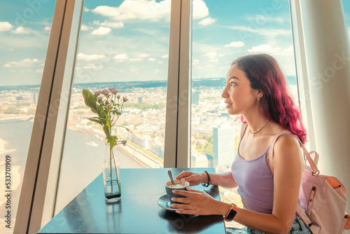 Happy girl drinking coffee in a cafe and admires out of the window on the observation deck of the TV Tower in Dusseldorf. Great viewpoint for tourists in Germany photo