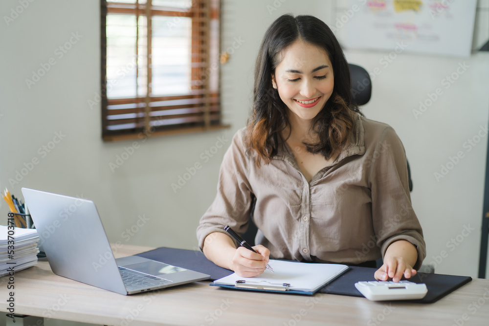 Portrait of a beautiful Asian woman looking at laptop screen while sitting at working desk in the office Portrait of a beautiful Asian woman looking at laptop screen while sitting at working desk in the office