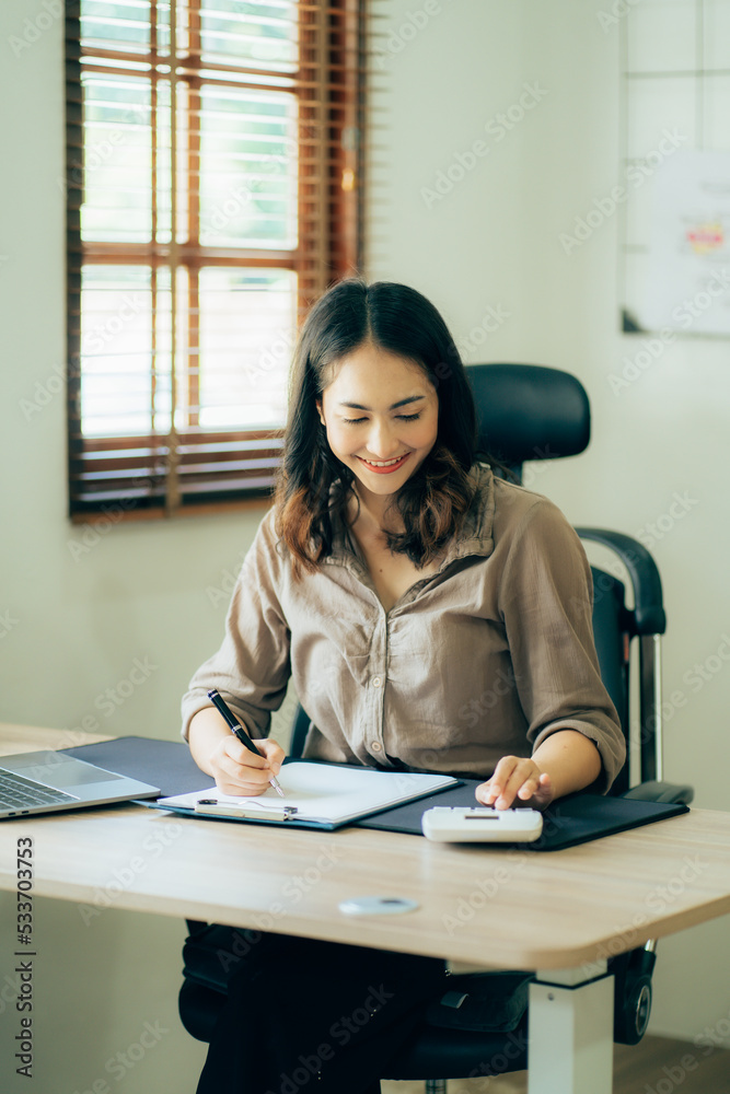 Portrait of a beautiful Asian woman looking at laptop screen while sitting at working desk in the office Portrait of a beautiful Asian woman looking at laptop screen while sitting at working desk in the office