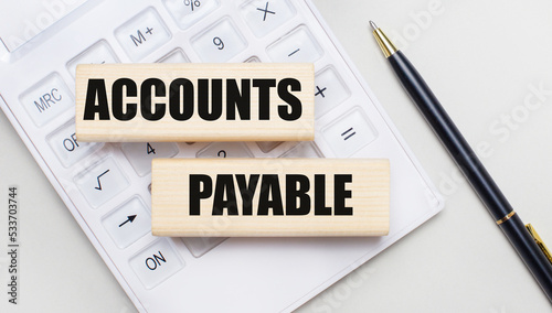 Wooden blocks with the ACCOUNTS PAYABLE Iie on a light background on a white calculator. Nearby is a black handle. Business concept