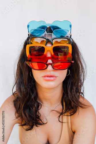 Young woman wearing various sunglasses in front of white wall