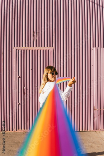 Young woman looking over shoulder holding rainbow colored ribbon in front of corrugated wall