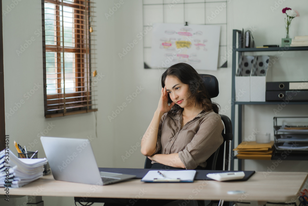 Portrait of a beautiful Asian woman looking at laptop screen while sitting at working desk in the office Portrait of a beautiful Asian woman looking at laptop screen while sitting at working desk in the office