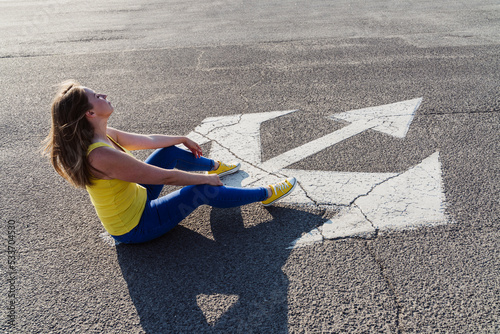Carefree woman sitting by three way direction arrow sign on road