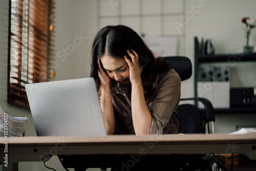 Portrait of a beautiful Asian woman looking at laptop screen while sitting at working desk in the office