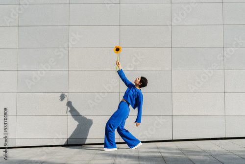 Woman with sunflower bending over backwards in front of wall on sunny day photo