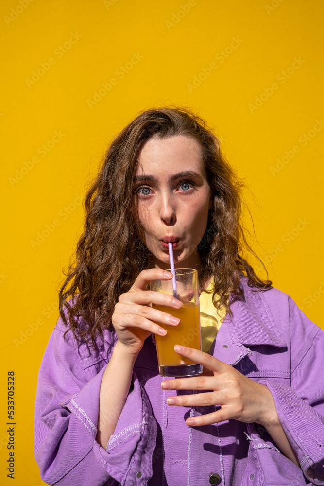 Woman with brown hair drinking juice in front of yellow wall Woman with brown hair drinking juice in front of yellow wall