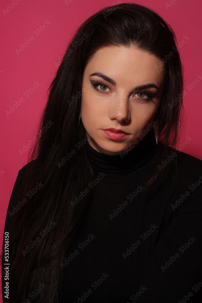 Portrait of a beautiful fashion glamour girl brunette in black clothes in the studio with big earrings on the pink background