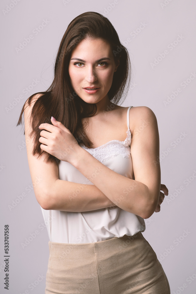 Beautiful woman fashion studio portrait with long dark hair and day make-up with seductive look and pose with crossed arms. Model wearing white blouse and beige trousers. Toned image with pink color Beautiful woman fashion studio portrait with long dark hair and day make-up with seductive look and pose with crossed arms. Model wearing white blouse and beige trousers. Toned image with pink color
