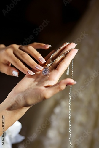 Women's hands of the bride in a wedding dress with a pendant. Jewelry for the bride.
