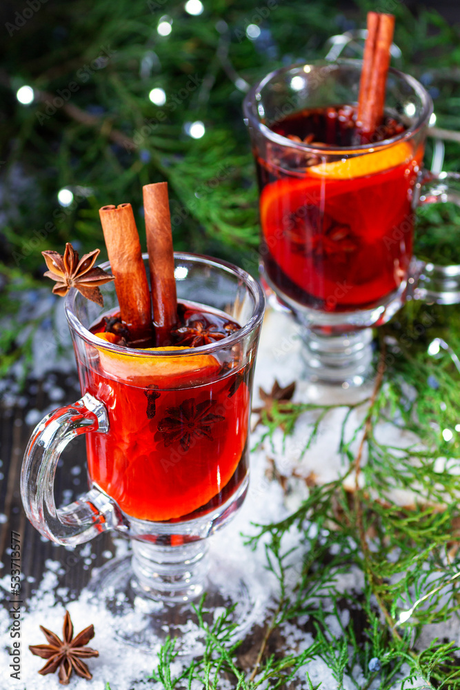 mulled wine with spices in glasses on a rustic wooden background among the branches of the Christmas tree and Christmas decor. A warming winter drink in a cup is standing in the snow. mulled wine with spices in glasses on a rustic wooden background among the branches of the Christmas tree and Christmas decor. A warming winter drink in a cup is standing in the snow.