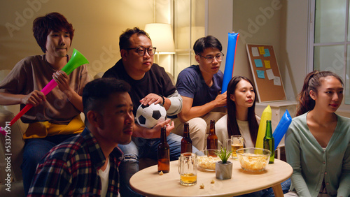Happy Asian people with friends watching soccer or football on tv and celebrating victory at home, world cup football cheering concept