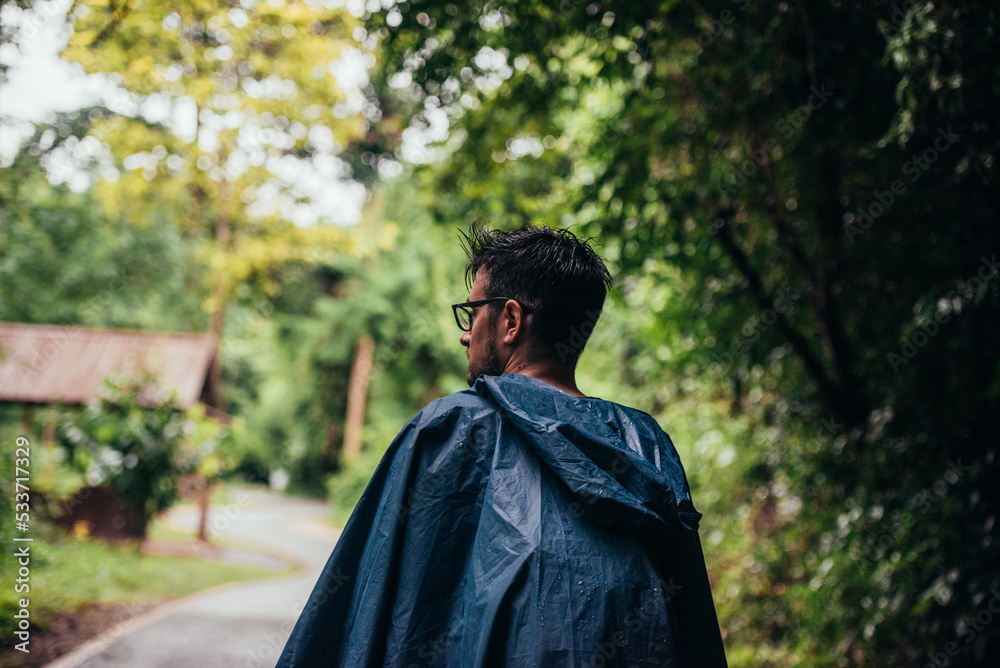 Man wearing a raincoat walking in the middle of a road next to the forest Man wearing a raincoat walking in the middle of a road next to the forest