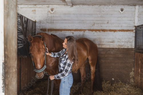 Fototapeta Naklejka Na Ścianę i Meble -  Woman brushes her horse in stables
