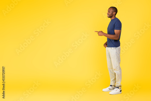Side View Of African Male Pointing Finger Aside, Yellow Background