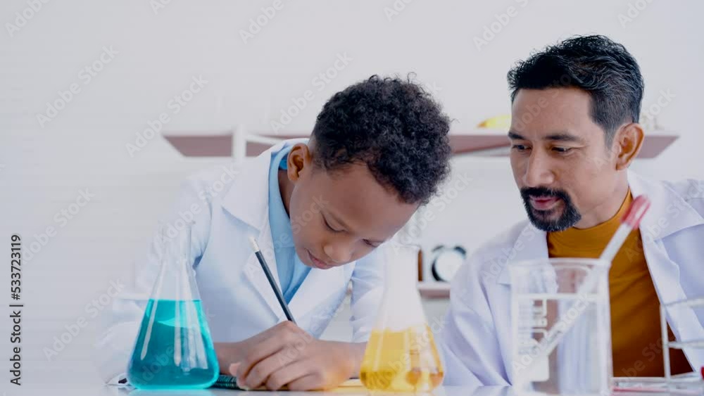 4K, Asian mixed-race boy is interested in science and takes notes on advice of teacher in the primary school's white science room. Concept education, Science experiments, Chemistry, Children 4K, Asian mixed-race boy is interested in science and takes notes on advice of teacher in the primary school's white science room. Concept education, Science experiments, Chemistry, Children