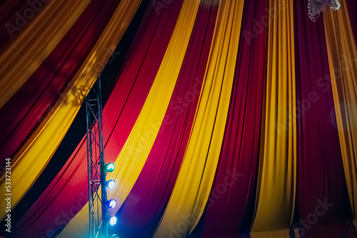 Ceiling decorated with heavy fabrics and light bulbs to show a circus feeling. Colorful curtain and light bulb decorations. Circus party decorations. Circus tent from inside.