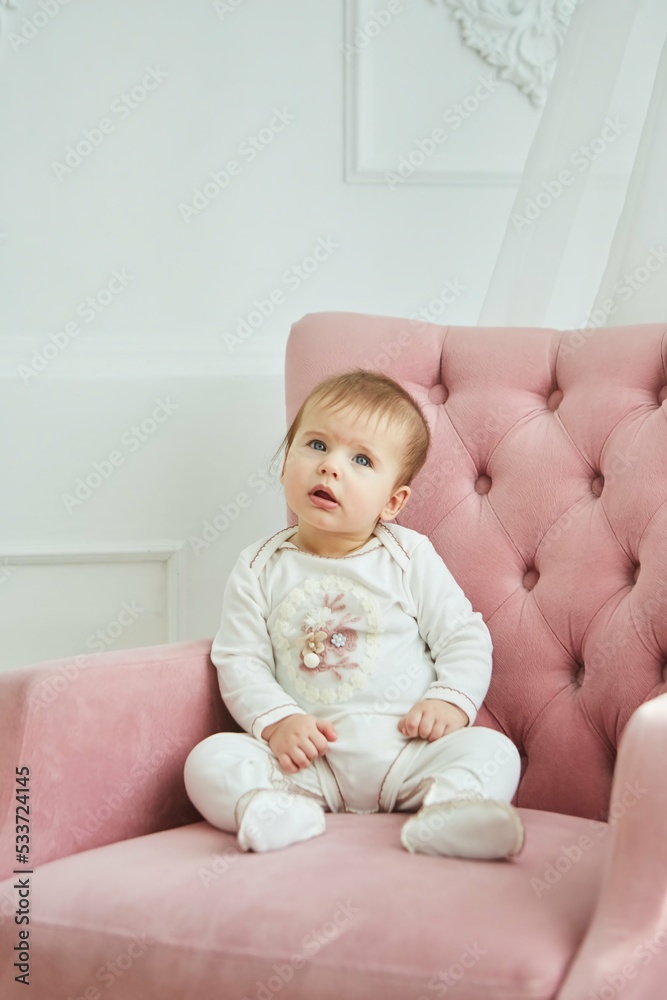 A little baby girl in white clothes is sitting on a chair. The concept of motherhood and childhood. A little baby girl in white clothes is sitting on a chair. The concept of motherhood and childhood.