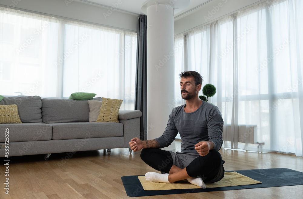 Young man cancer survivor practicing home workout yoga training, stretching muscles and breathing exercise for healthy life after long struggle with sickness and pain. Young man cancer survivor practicing home workout yoga training, stretching muscles and breathing exercise for healthy life after long struggle with sickness and pain.