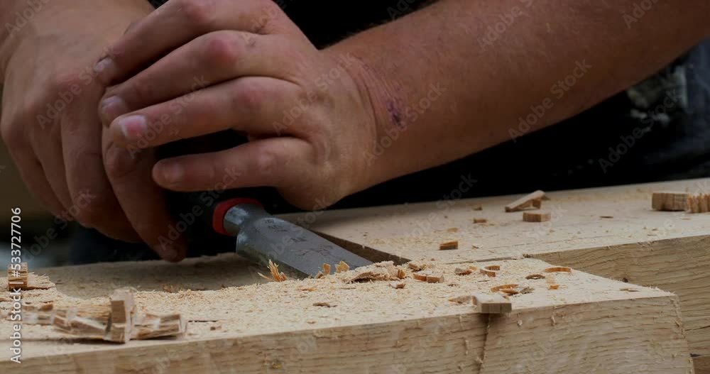 Close up detail of carpenter chiseling a wooden beam for log cabin construction in the mountains