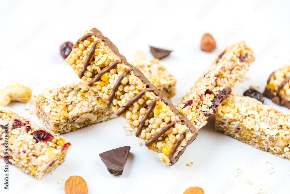 Close view of various homemade granola bars with nuts, seeds, dark chocolate, honey and berries over a white background.
