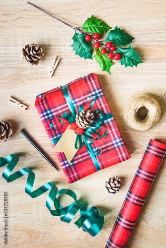 Obraz na płótnie Flat lay of a Christmas gift box wrapped in scottish tartan pattern paper with wrapping materials over a wooden background. Christmas presents preparation. w salonie