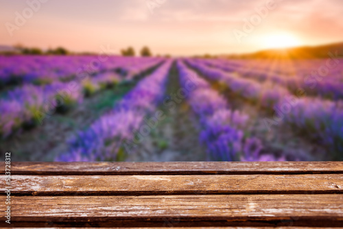 Empty wooden table in front of a blurred blooming lavender field under the golden colors of the summer sunset. Product display montage.