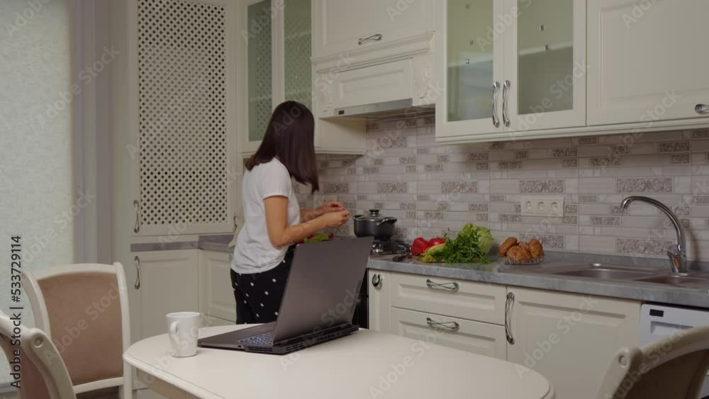 Businesswoman finishing soup then sitting in front of laptop at kitchen table. Part-time job working online. Remote working. Businesswoman finishing soup then sitting in front of laptop at kitchen table. Part-time job working online. Remote working.