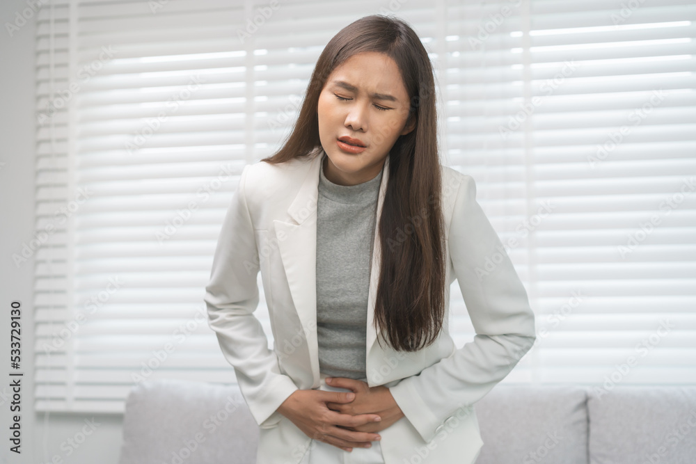 Flatulence, abdomen asian young business woman in suit at home, hand in stomach ache, expression face suffer from food poisoning, abdominal pain and colon problem, gastritis or diarrhoea, inflammation Flatulence, abdomen asian young business woman in suit at home, hand in stomach ache, expression face suffer from food poisoning, abdominal pain and colon problem, gastritis or diarrhoea, inflammation