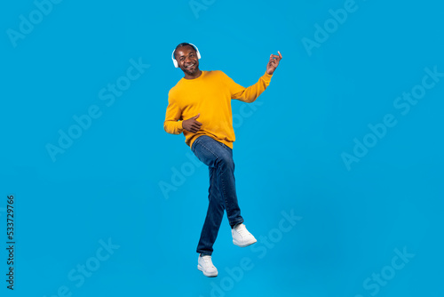 Positive black man listening to music and dancing, using headphones